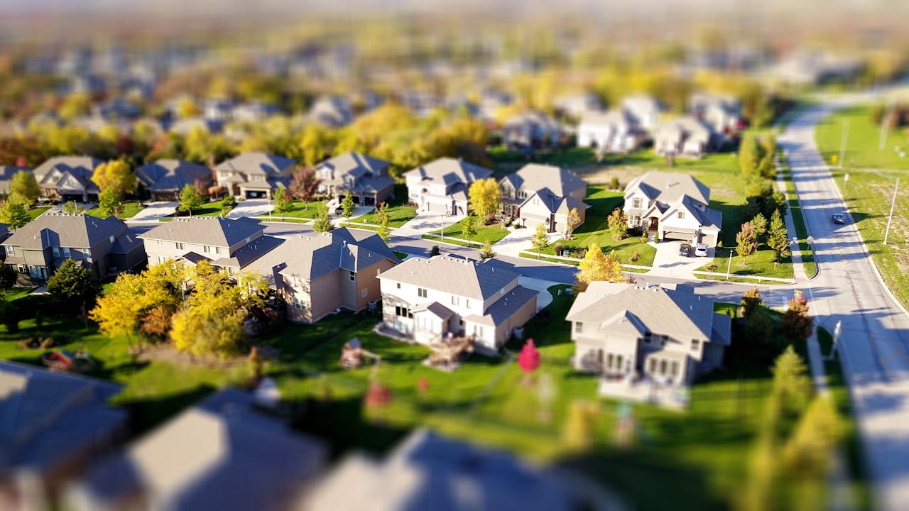 services-01 Tilt-shift aerial photo of a suburban neighborhood with green lawns and roads.